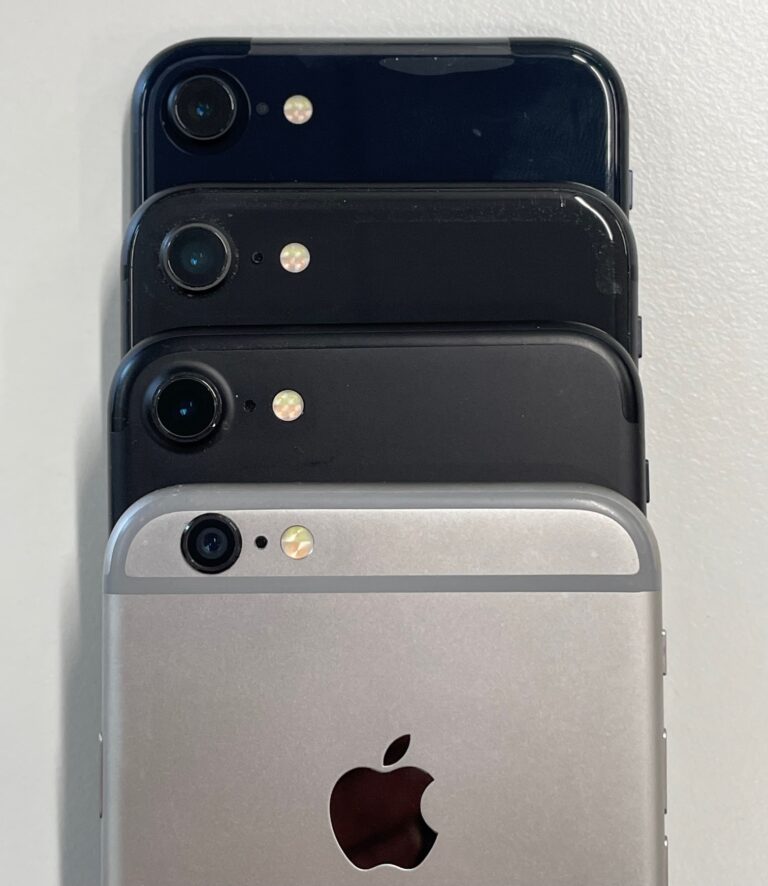Iphones - models 6, 7, 8 and SE2 - stacked for comparison. These models have nearly identical case shape and dimensions. View of the back side top section, showing: camera, microphone hole, dual-tone LED illuminator. 6 and 7 have aluminium backs whilst 8 and SE have glass. iPhone 6 is "space grey" colour, others are black or "midnight". The SE 2nd gen is new out of box and still has protective shipping wrapper attached; others are used and showing some wear.
