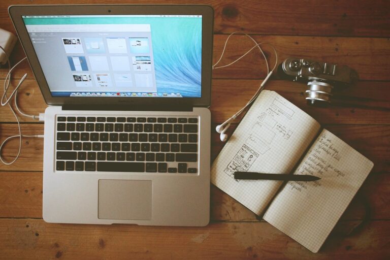 Apple Laptop Computer with Headphones, Camera, and Open Notebook